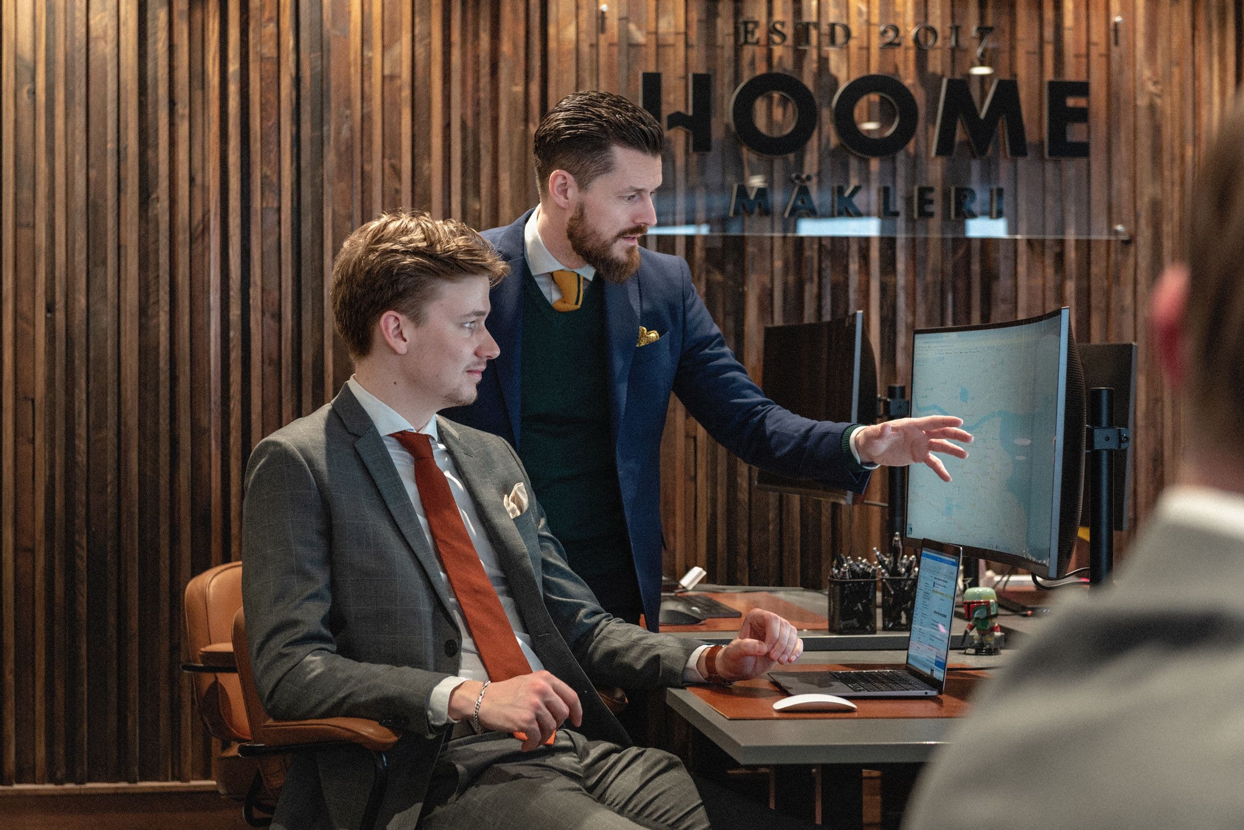 Två mäklare vid en skrivbord som tittar på en skärm och diskuterar