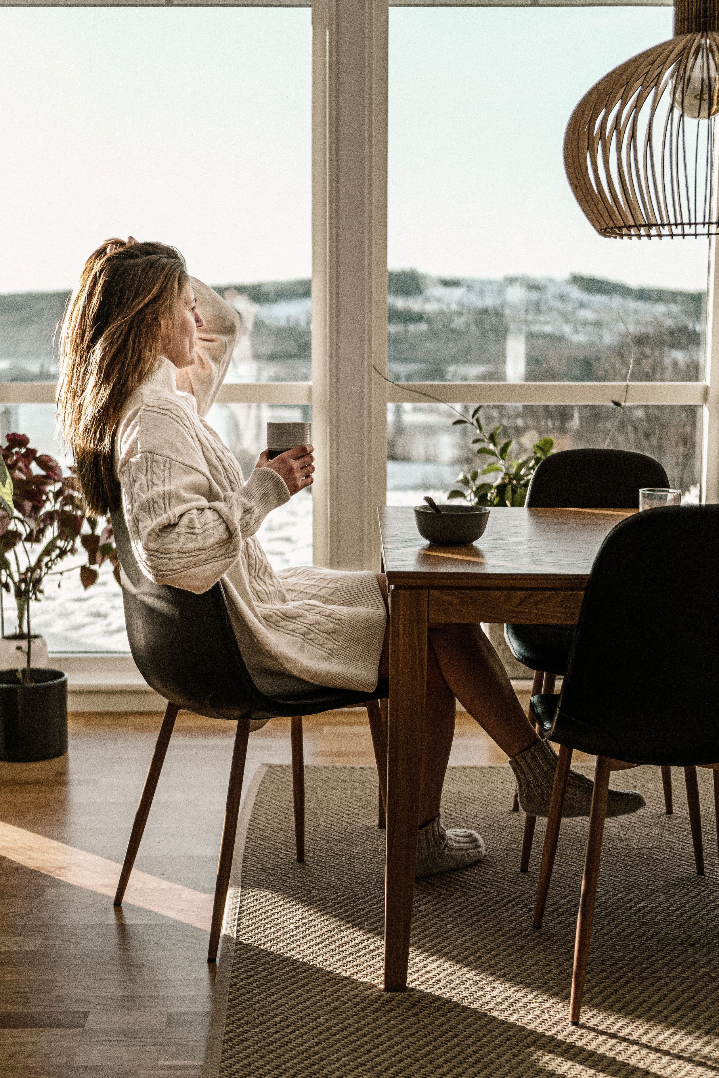 Kvinna vid matbord med kaffekopp som blickar ut genom fönstret
